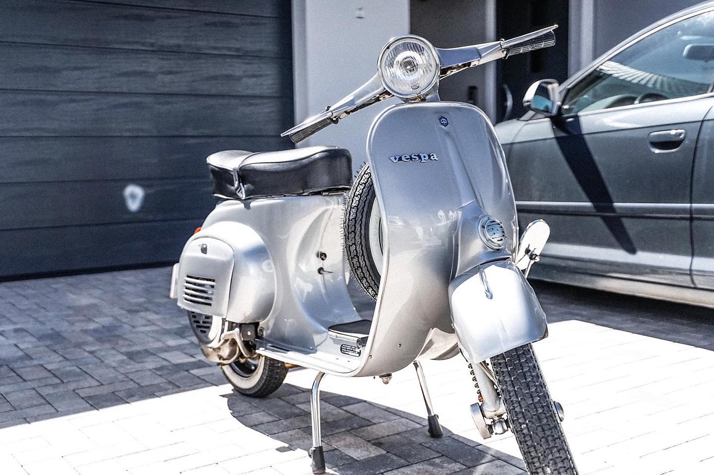 Oldtimer-Aufbereitung: Silberner Vespa-Roller nach der Aufbereitung vor einem Garagentor, Lack und Chrom glänzen wieder