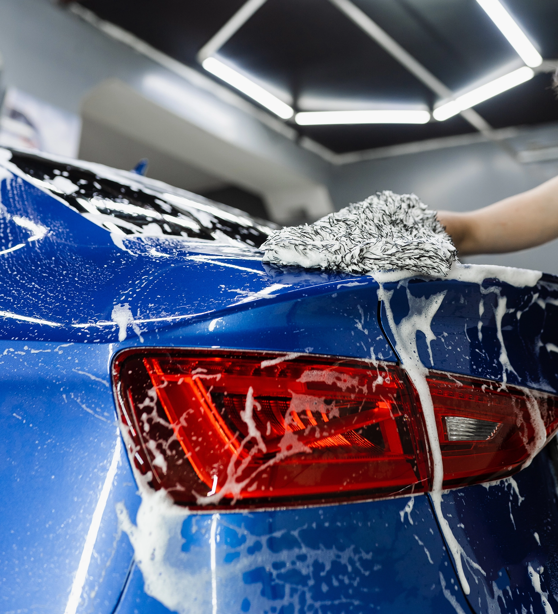 Außenreinigung: Heck eines blauen Autos wird mit Waschhandschuh und Schaum gewaschen