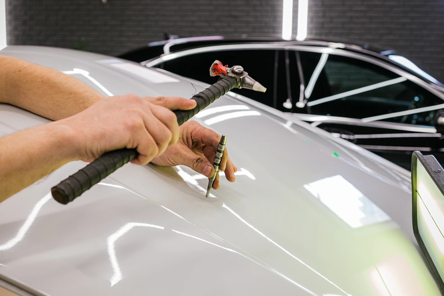 Dellenentfernung ohne Lackieren: Eine Delle in der silbernen Motorhaube wird mit Klopfhammer und Ausbeulstift vorsichtig ausgeklopft