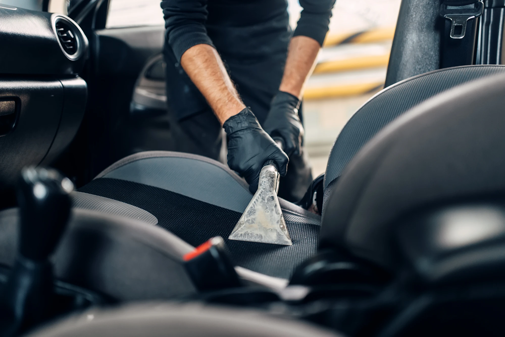 Innenraumreinigung: Autositz wird mit Absaugdüse gereinigt