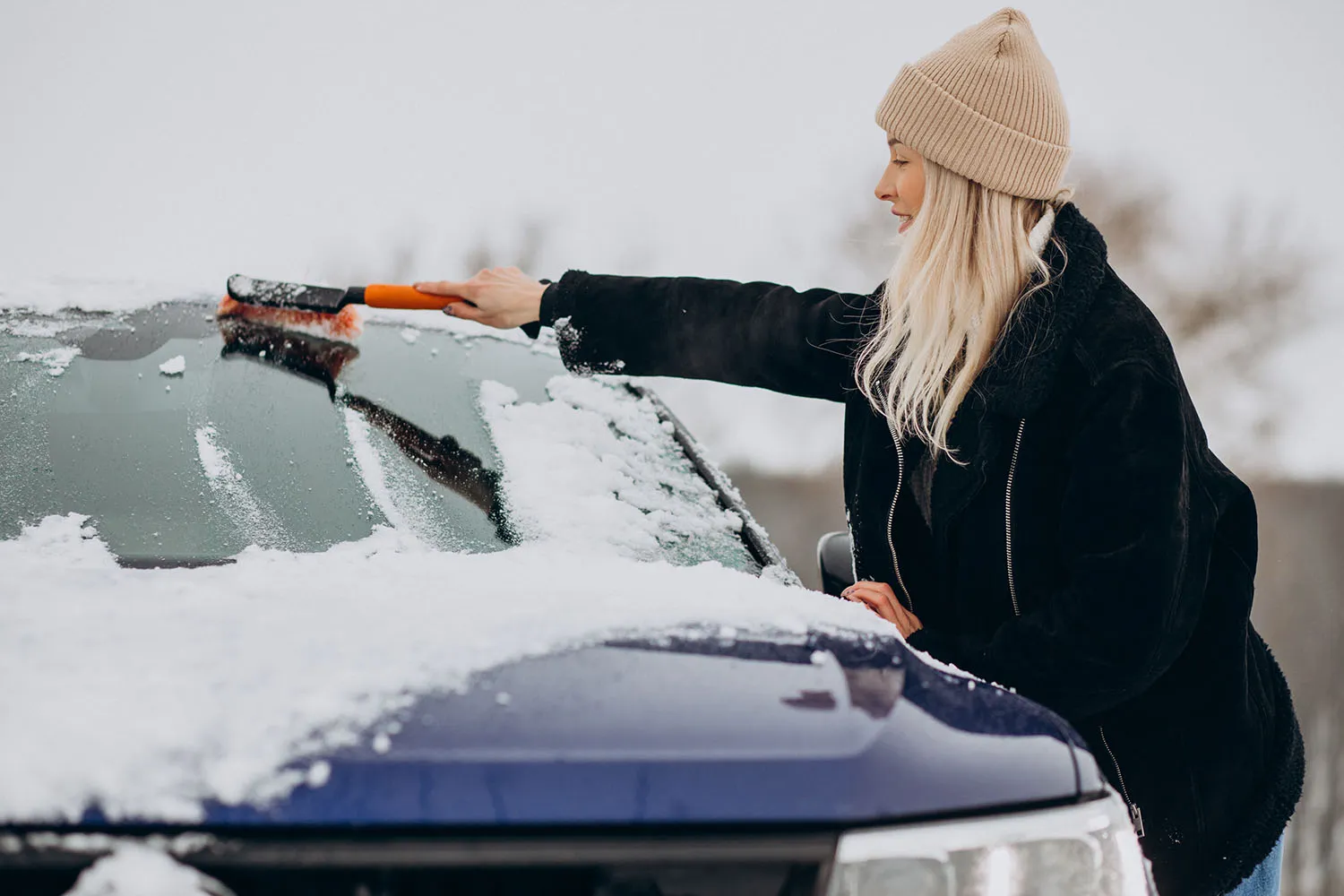 Scheibe enteisen: Frau befreit die Frontscheibe ihres Autos mit einem Schneebesen von Schnee und Eis